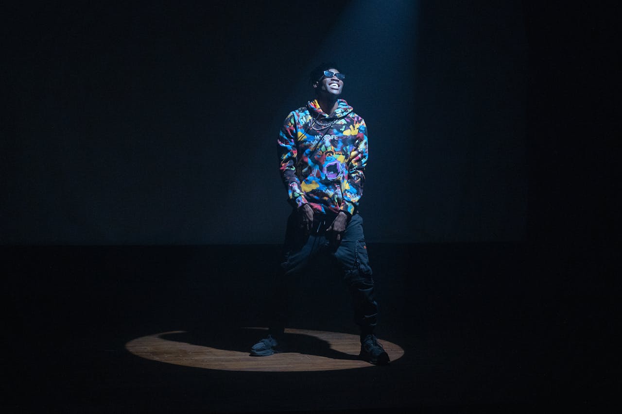 Energetic hip hop musician in colorful attire illuminating the stage under a dramatic spotlight.